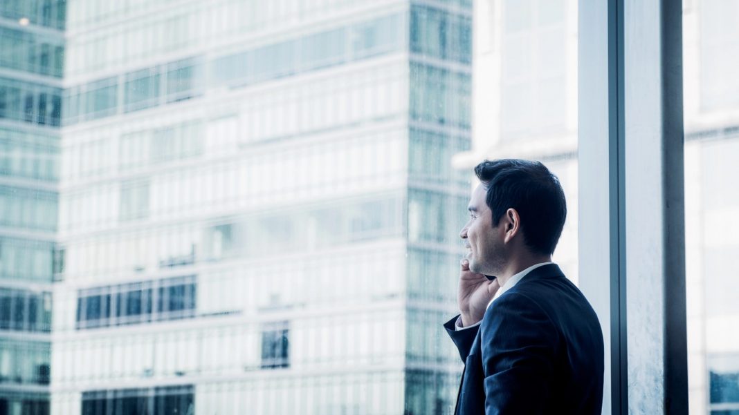 Businessman using mobile phone near office window at office.