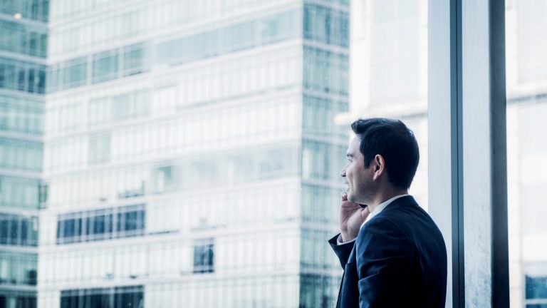 Businessman using mobile phone near office window at office.