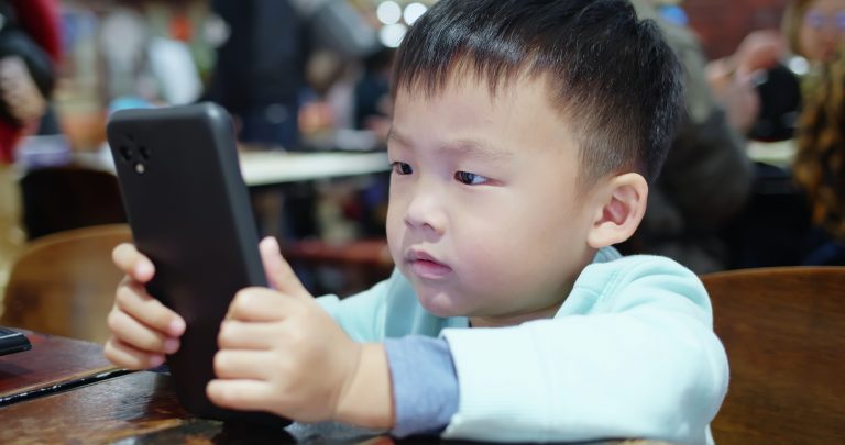 Asian boy play mobile phone very intently when going out